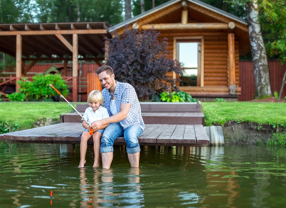 Personal Insurance - Father and Young Son Sit on Dock Fishing in Front of Their Lake House
